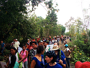 A crowded group of people walking along a path surrounded by lush greenery. The crowd includes men, women, and children.