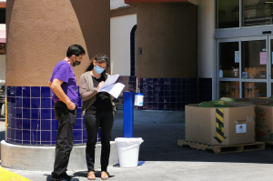 2 people are standing outside a store, discussing some papers.