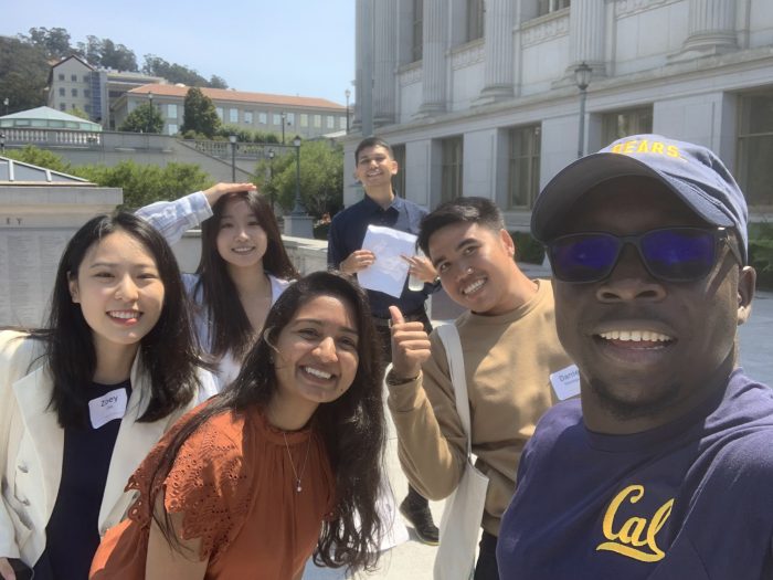 A group of six incoming Third Cohort students smiling for a selfie, standing near Doe library.