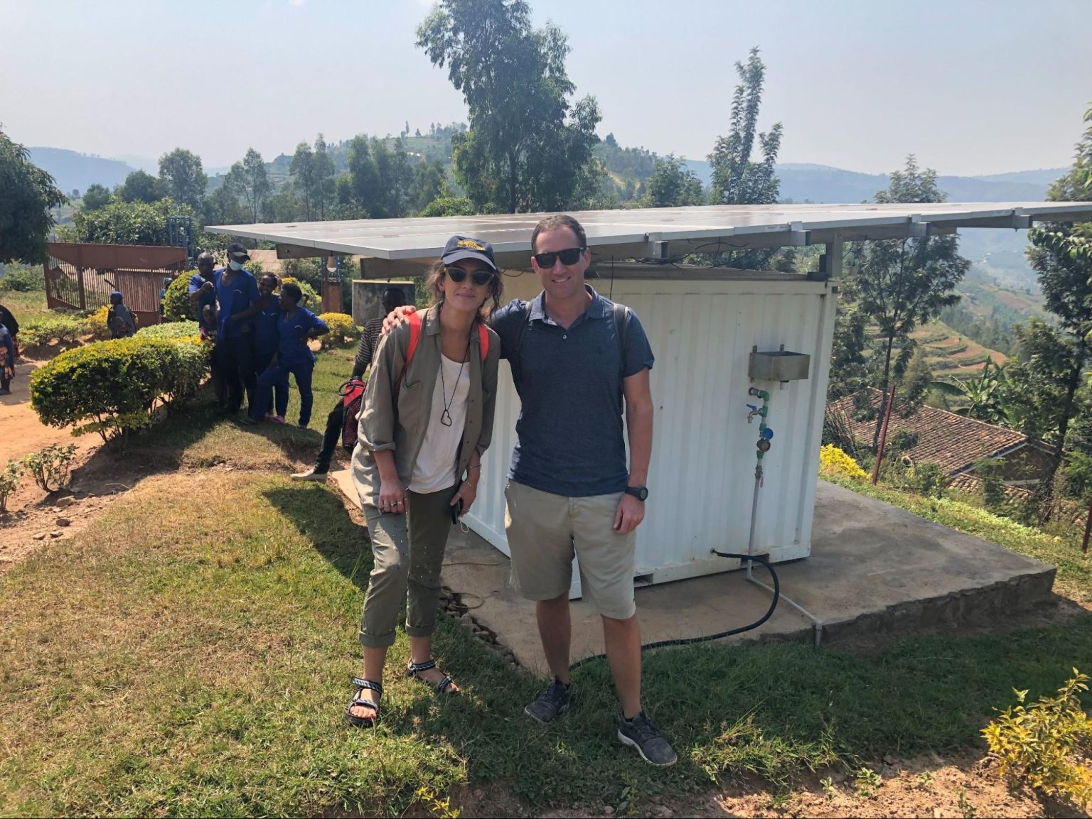 Ingrid Xhafa and Greg Berger in Rwanda posing near the white off-grid solar-power system