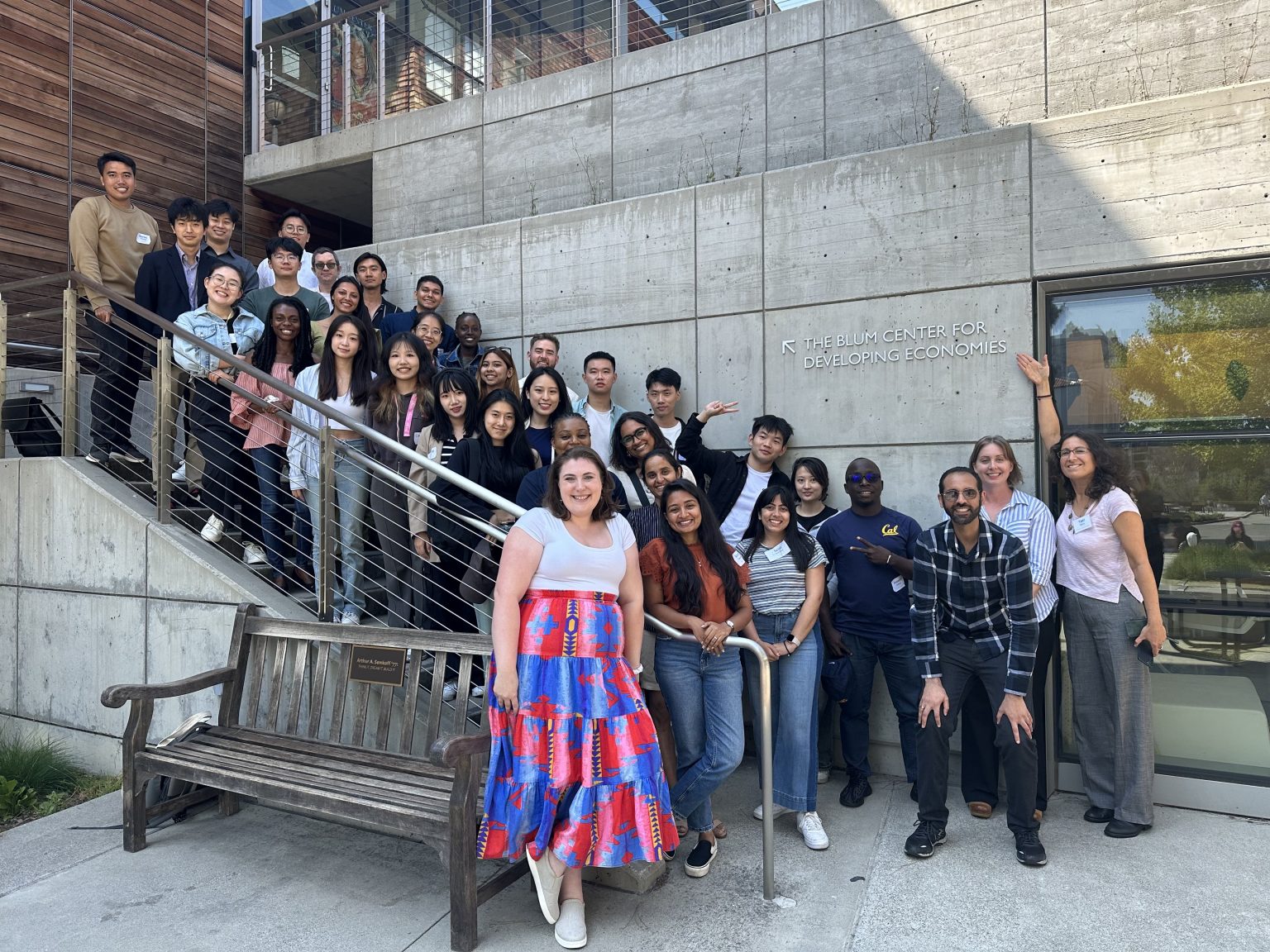 The Master of Development Engineering’s Class of 2024 gathered outside the Blum Center for Developing Economies. They are standing on and around a staircase, posing for a group photo. The participants are diverse, with a mix of ages and backgrounds, smiling and appearing enthusiastic.